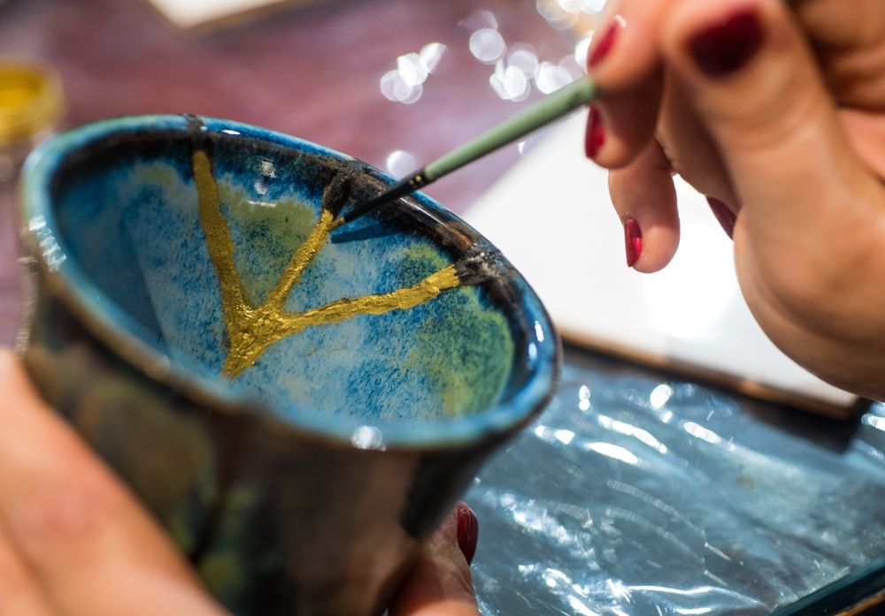 Kintsugi, a japán koncepciók leghíresebbje. Női kéz kerámiát javít aranyfestékkel.